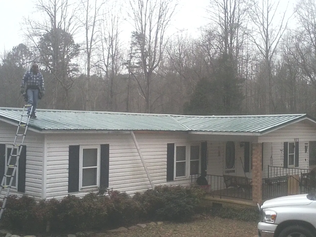 Worker on a ladder beside a new green metal roof on a ranch home in Sneedville