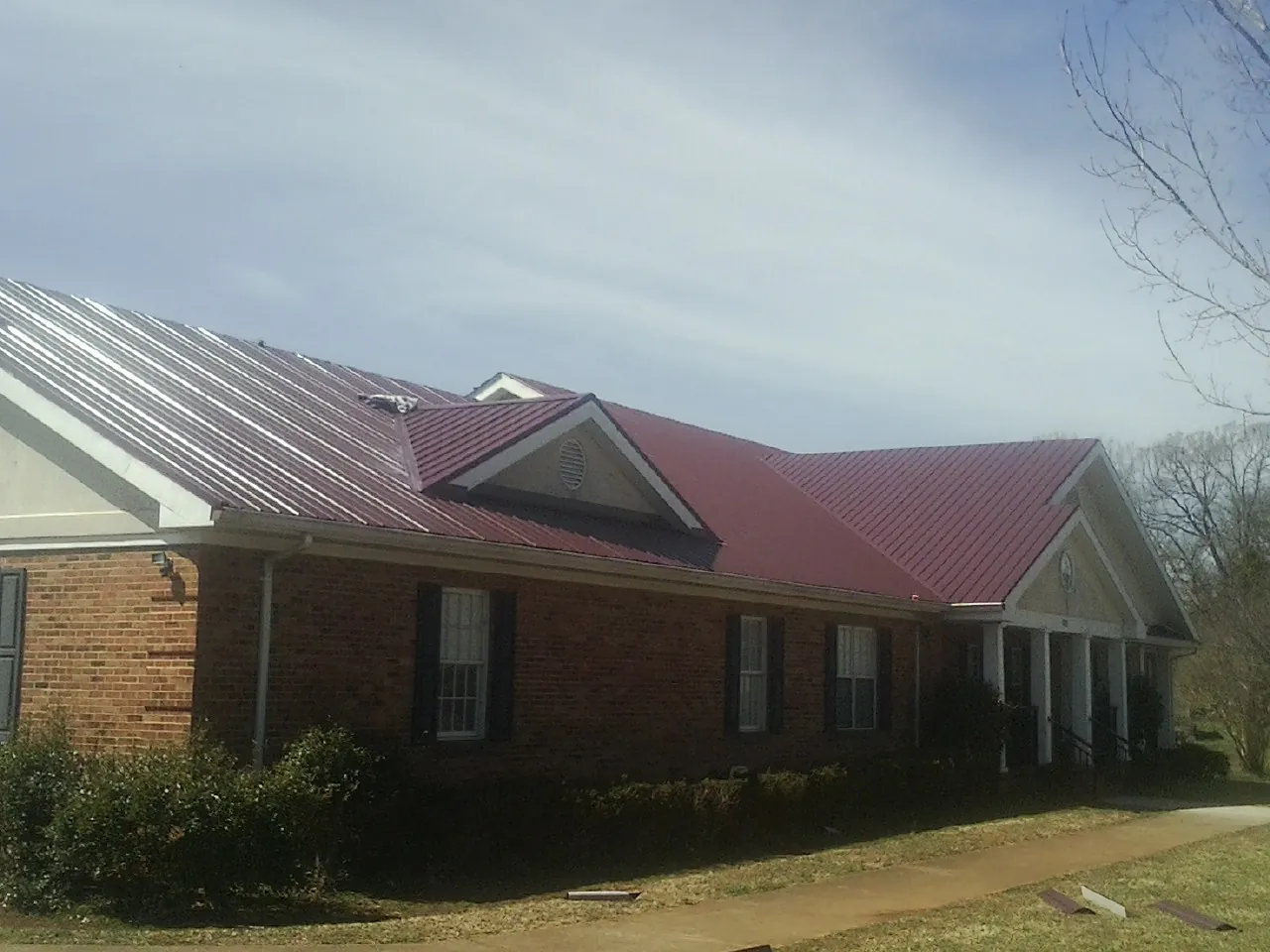Red metal roof with gabled entries on a long brick building, from a Hail Damage Roof Repair job in Sneedville