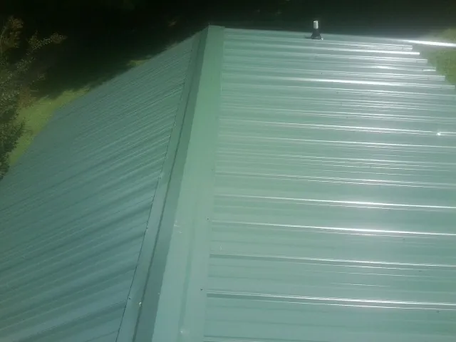 New green metal panels meeting at the ridge of a roof — Flat Roof Repair work by our crew in Sneedville