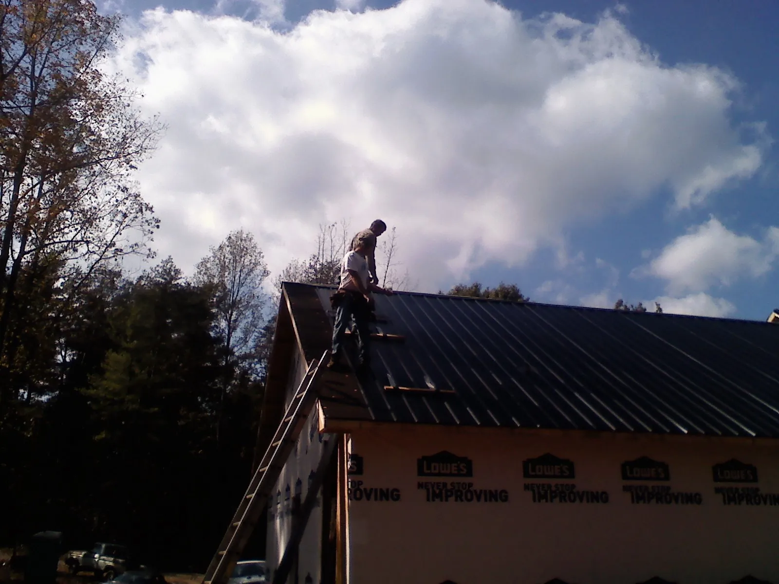 Roofer fastening dark metal panels high against a cloudy sky, from a Roof Inspection job in Sneedville