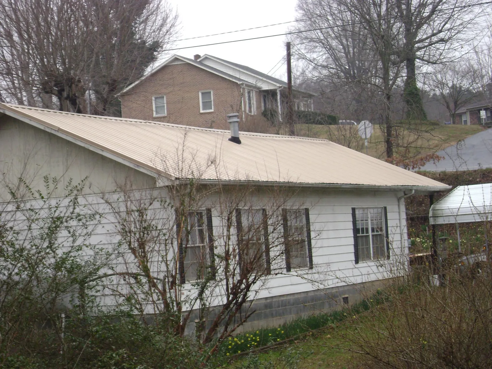 Tan metal roof on a white sided house set into a hillside — Commercial Roofing by Roofing Brothers in Sneedville
