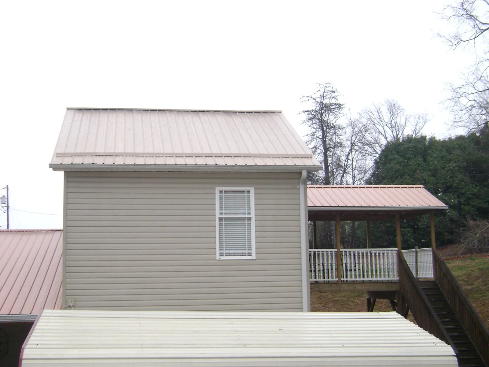 Tan metal roofs on a two story addition and attached porch, from a Roof Replacement job in Sneedville